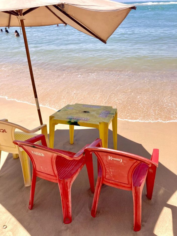 Tavolino e sedie rosse sotto un ombrellone sulla spiaggia, davanti al mare.
