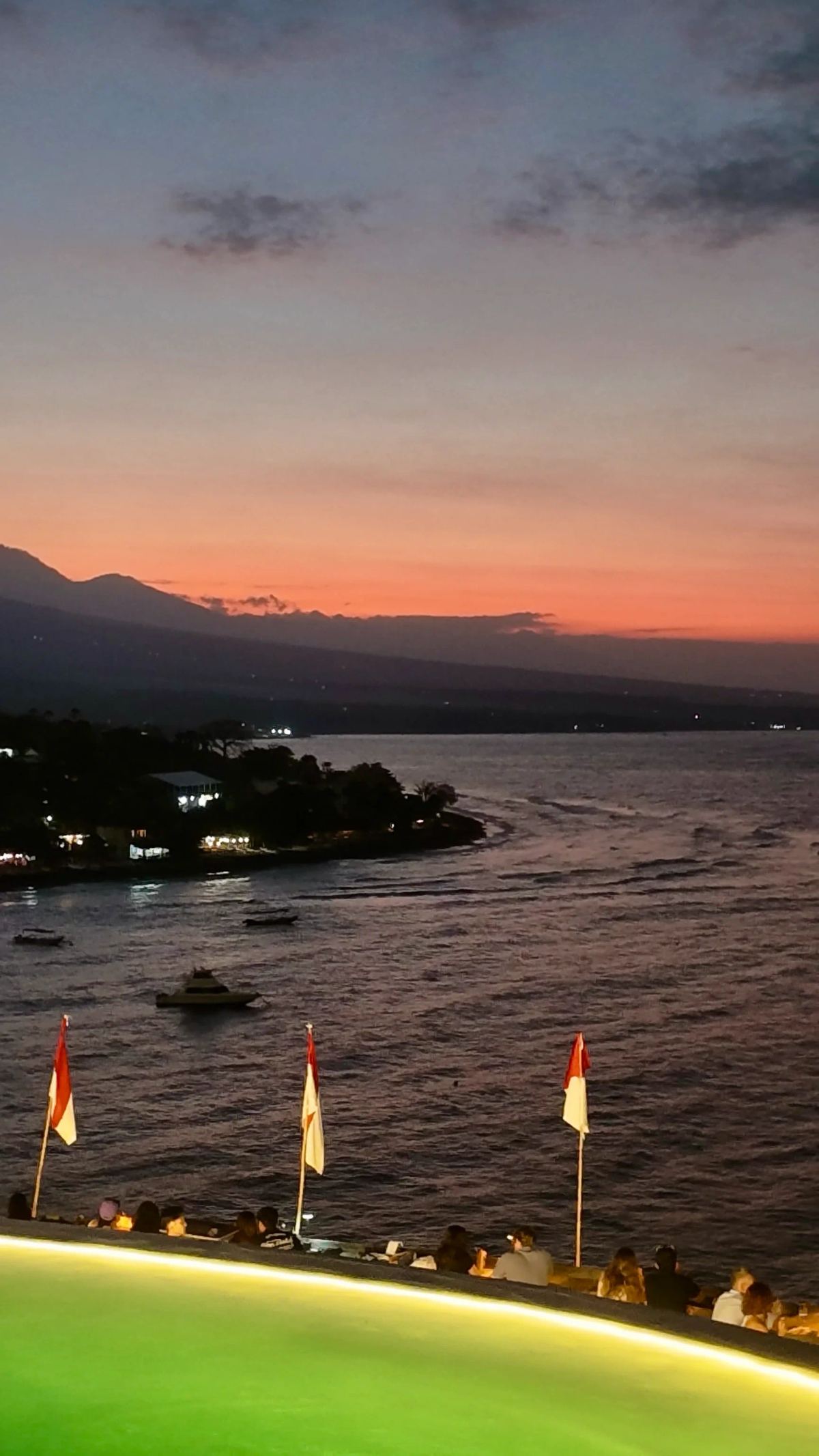 Tramonto sul mare di Amed con montagne, barche e bandiere indonesiane.