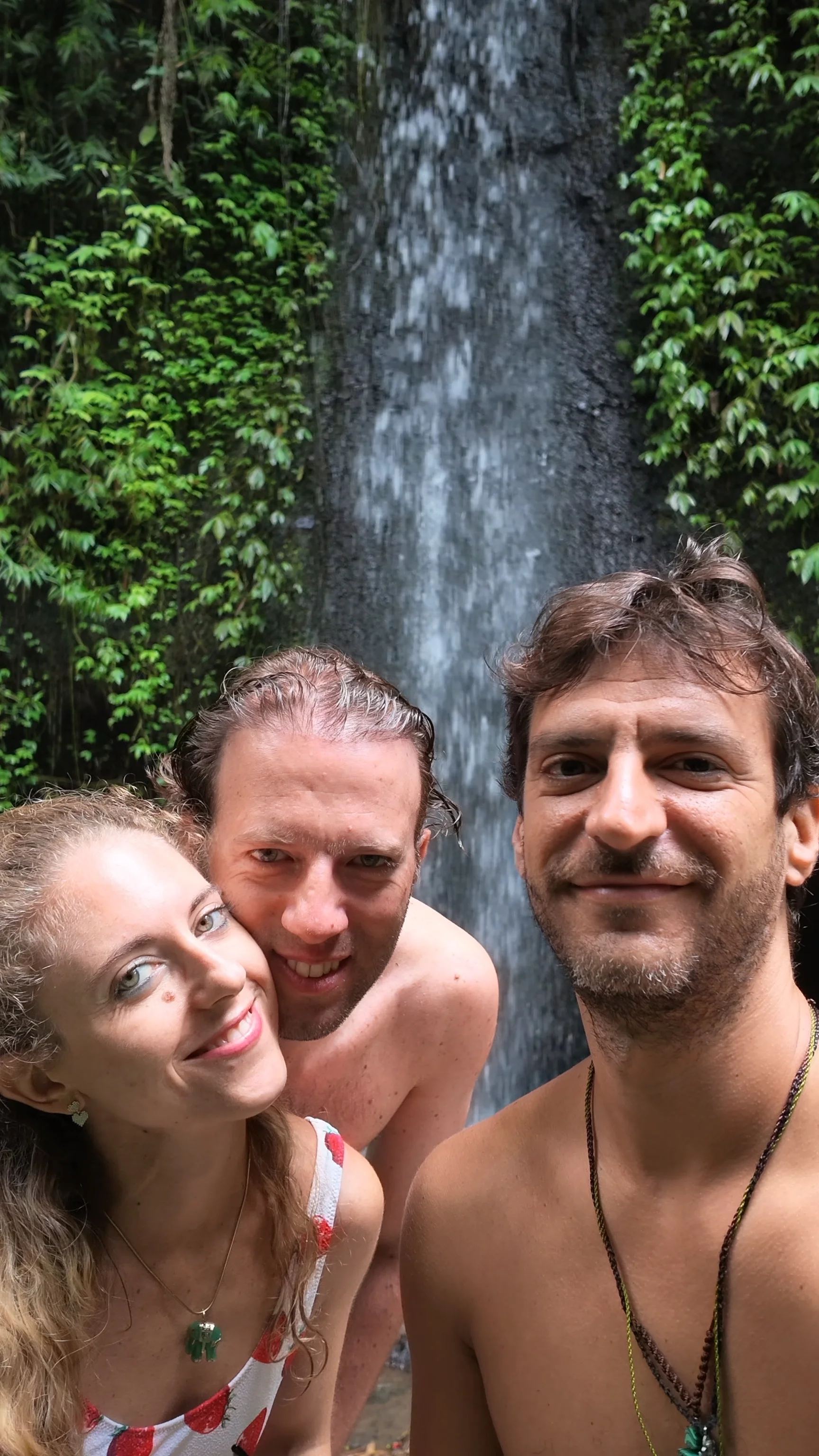 Tre viaggiatori davanti a una cascata immersa nella vegetazione.
