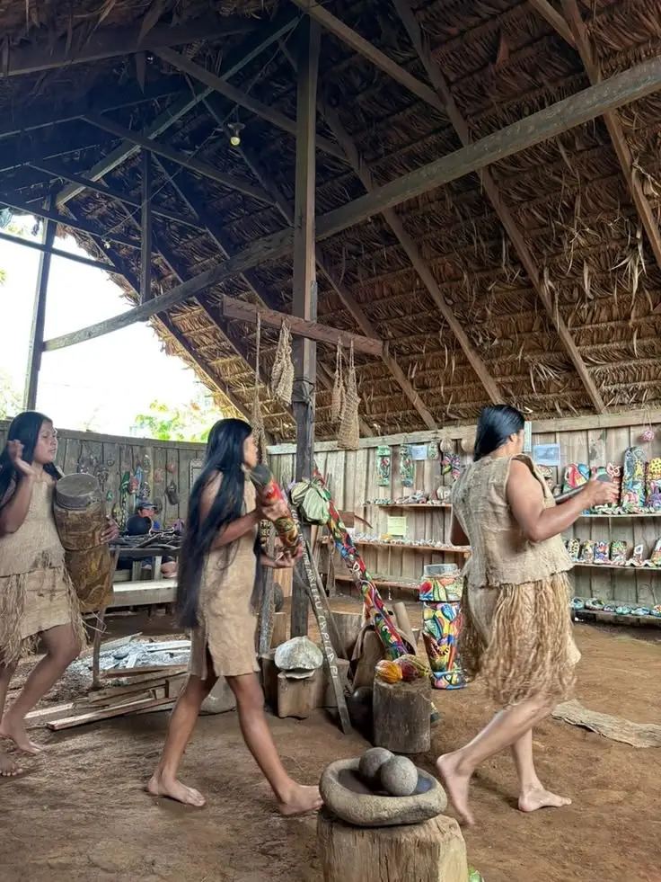 Donne di una comunità indigena danzano sotto una grande copertura di paglia