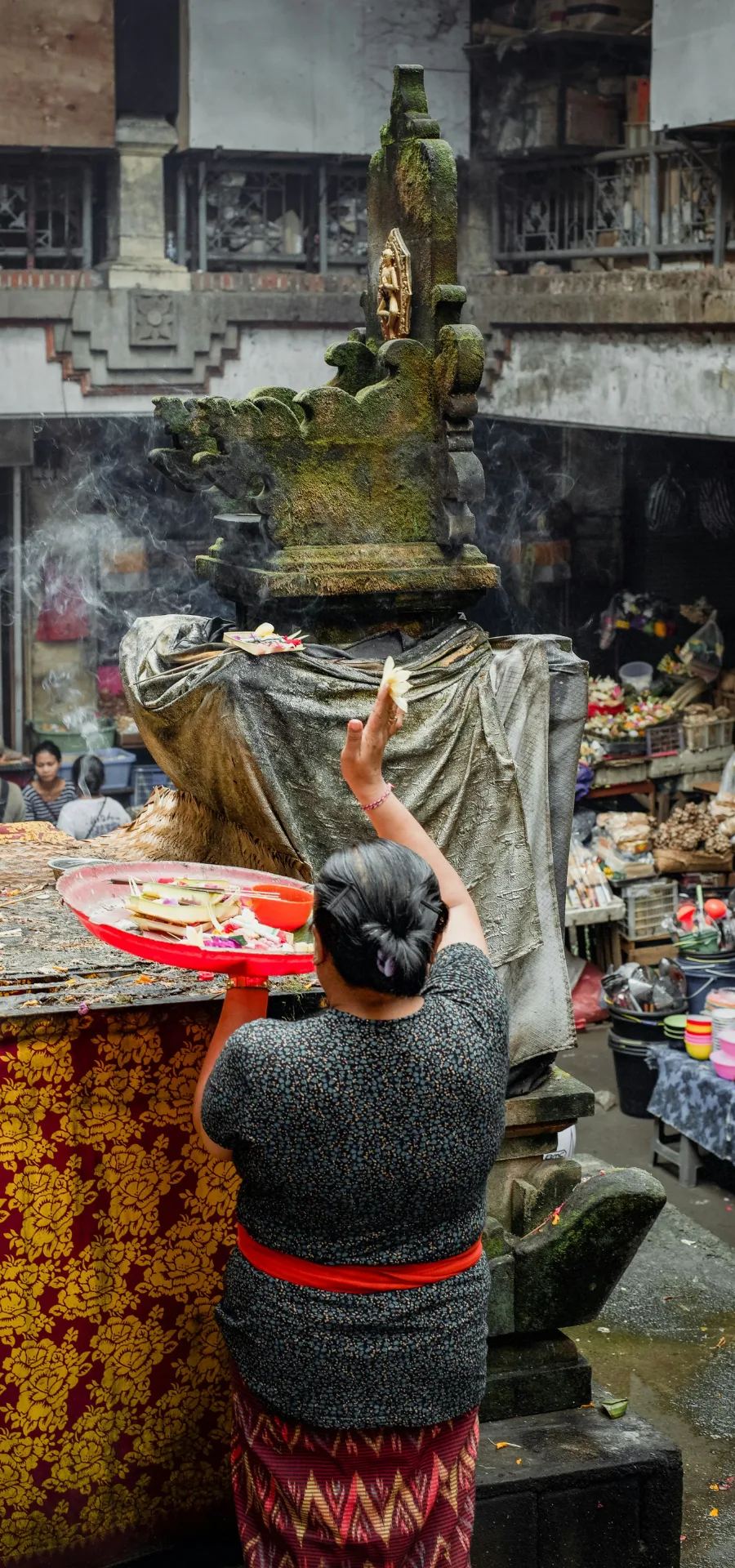 Una donna depone un'offerta davanti a una statua in un mercato di Ubud